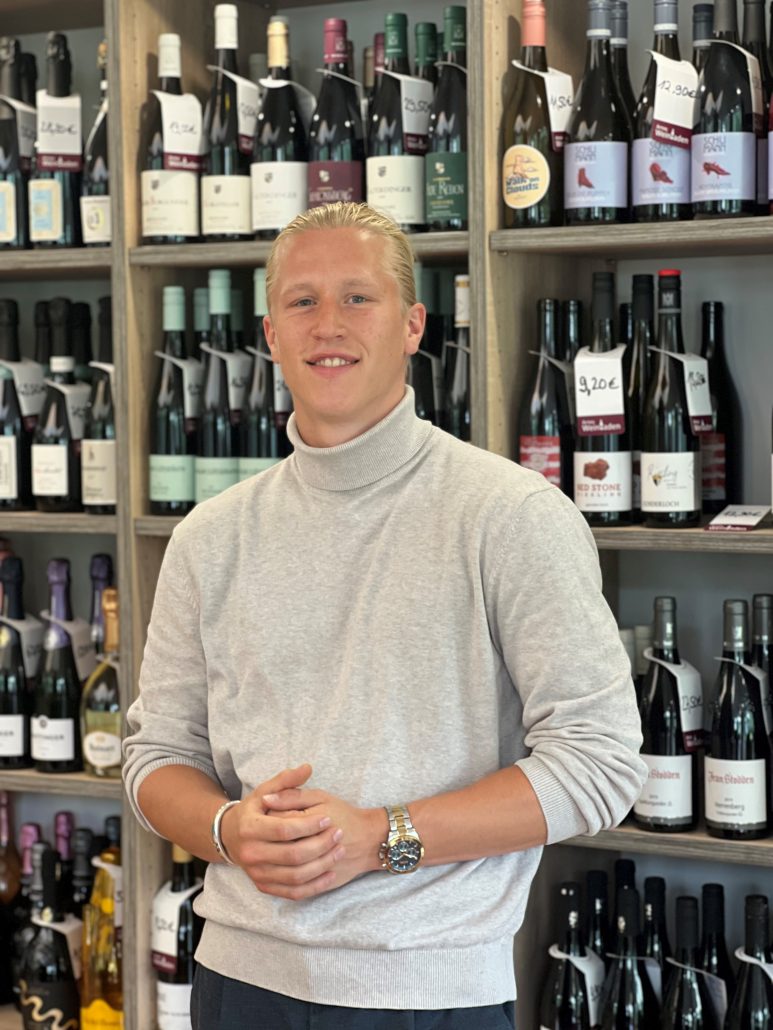 Noam Merlin Wagner im Weinladen vor dem Weinregal