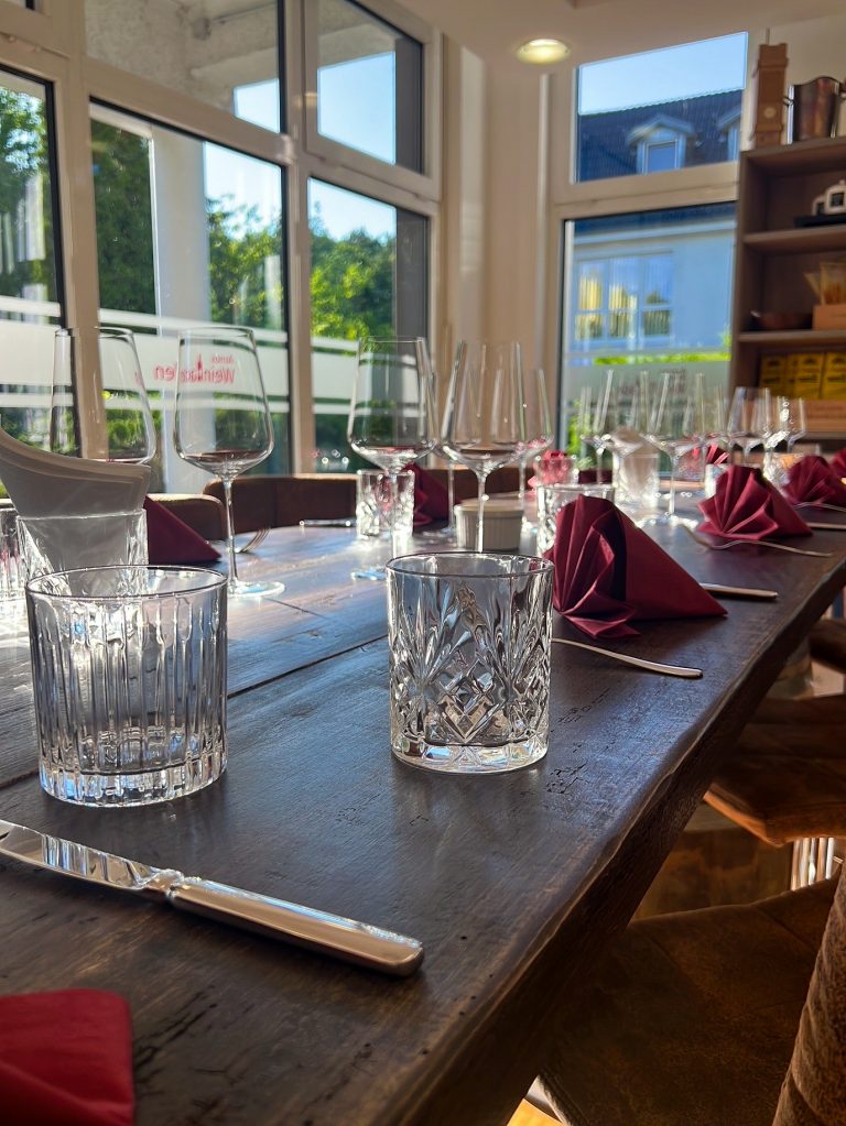 Gedeckte lange Tafel mit Weingläsern in Arnos Weinladen