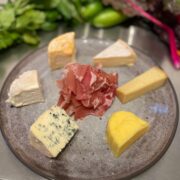 Teller mit sechs verschiedenen Käsesorten, darunter Blauschimmelkäse, und in der Mitte aufgeschichtetem rohem Schinken