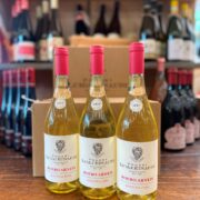 Drei Flaschen Poderi Luigi Einaudi Roero Arneis „Donna Ida“ Jahrgang 2025 stehen im Weinladen auf einem Holztisch