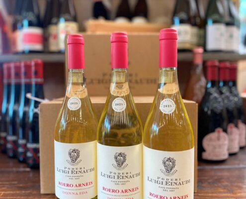 Drei Flaschen Poderi Luigi Einaudi Roero Arneis „Donna Ida“ Jahrgang 2025 stehen im Weinladen auf einem Holztisch