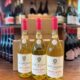 Drei Flaschen Poderi Luigi Einaudi Roero Arneis „Donna Ida“ Jahrgang 2025 stehen im Weinladen auf einem Holztisch